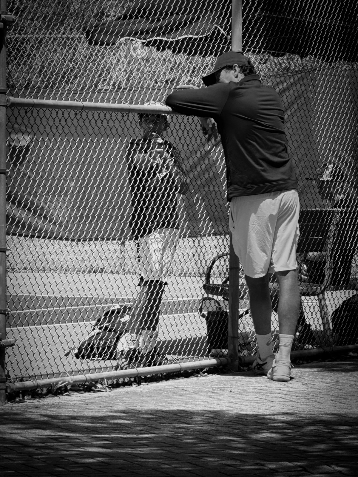 Shaan on court seen through the fence while his coach leans on the rail and talks to him